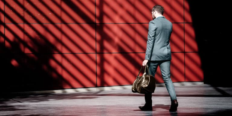 An investment executive with a brown bag walking towards a red building while talking on his phone.