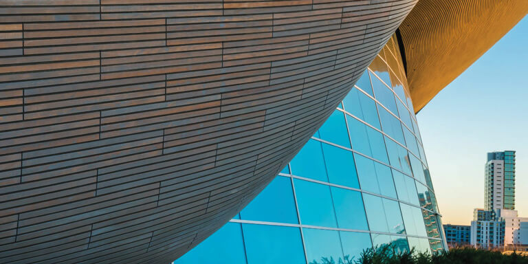 A futuristic, round, glass and steel office building with an abstract and asymmetric curved roof.