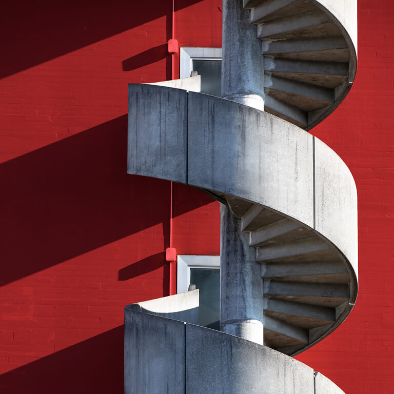 Spiral concrete staircase of red, minimalist building, symbolising a hypothetical climb up the corporate ladder.