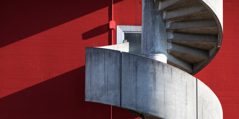 Spiral concrete staircase of red, minimalist building, symbolising a hypothetical climb up the corporate ladder.