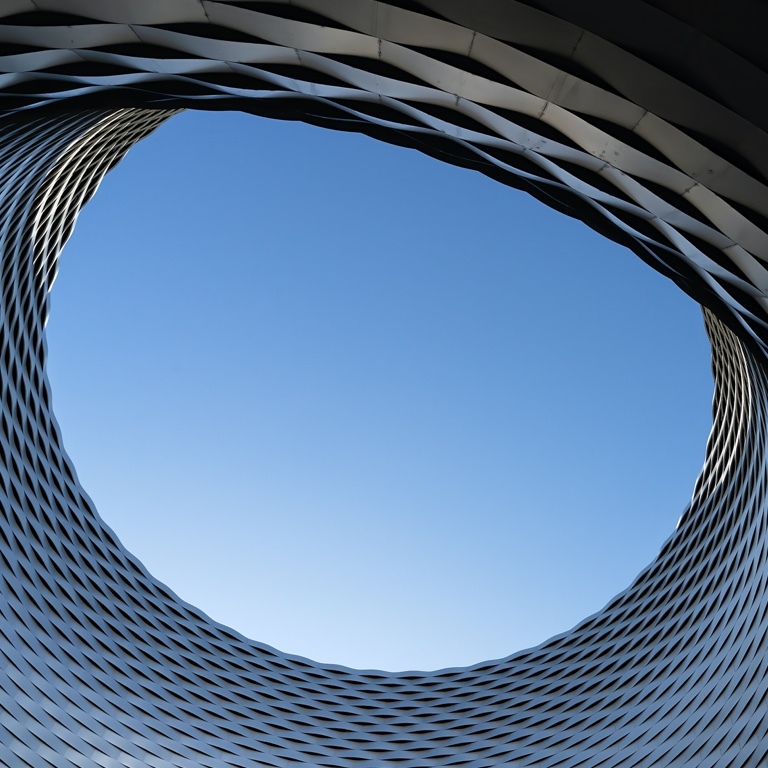 A shot of a clear blue sky, taken from the center of a circular, modern office building.