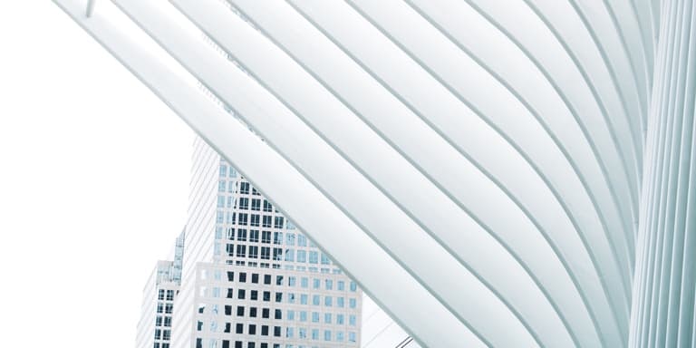 Soft, white concrete curves of a building in the forefront, with a skyscraper building in the background.