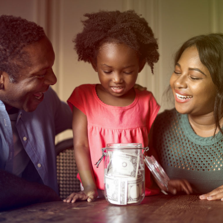 A couple and their daughter putting money into a jar.