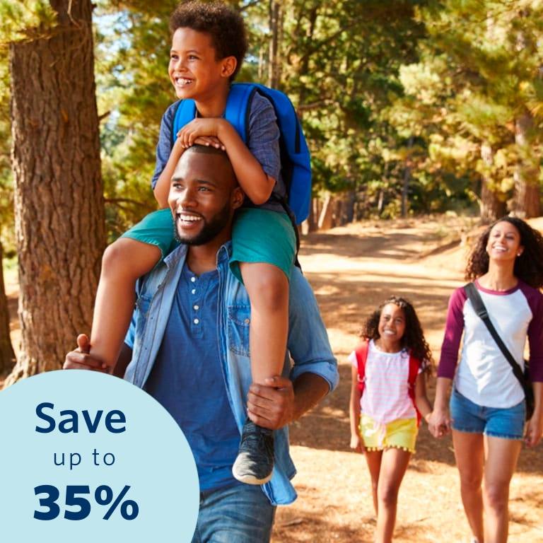 Young mom and dad are walking in the park. The dad is carrying his son on his shoulders.