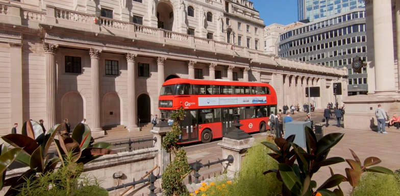 A red double decker tour bus parked nest to an old traditional-looking building on the streets of London.