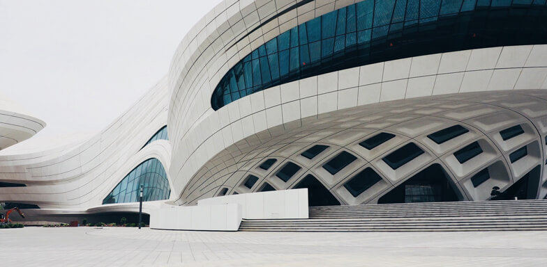 A modern, curved abstract white building, with a blue curved glass facade and a white staircase at the entrance.