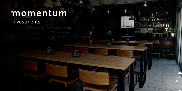 A wine cellar furnished with high wooden tables and chairs and a bar section.