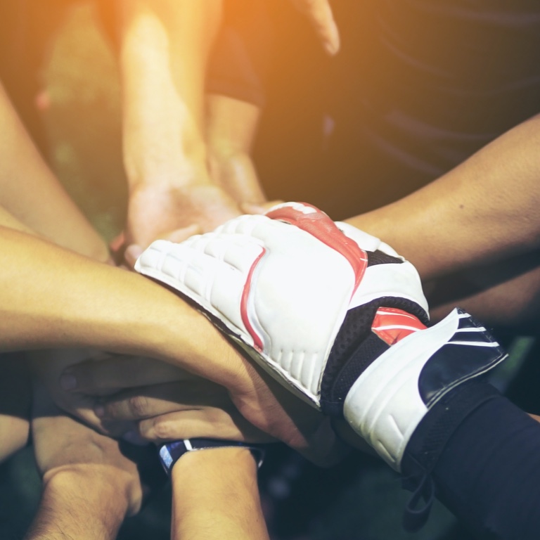 A closeup of a soccer team's hands joined together in a circle, with the goalie's gloved hand on top of the group's hands. 