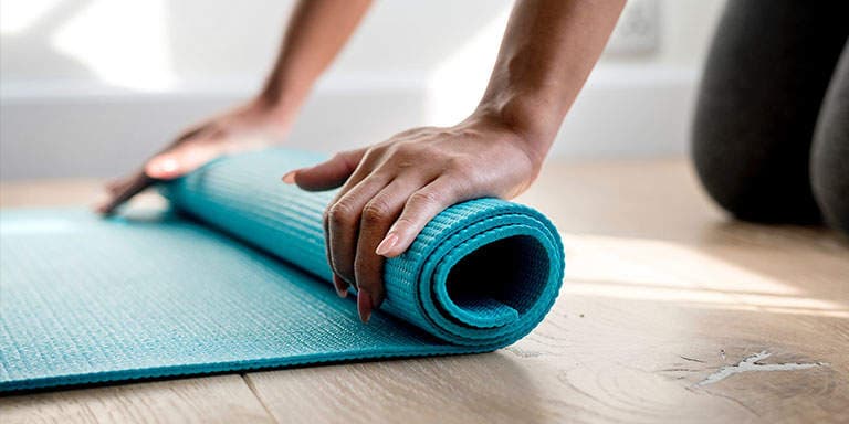 Young lady rolls up a blue yoga mat after a yoga fitness session.