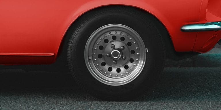 Close up detail of the tyre on a shiny red classic car parked on a tar road near a sidewalk.