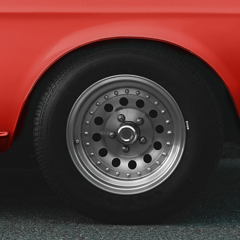 Close up detail of the tyre on a shiny red classic car parked on a tar road near a sidewalk.