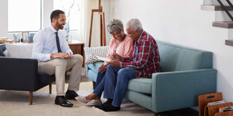 Elderly couple sitting on a couch going through financial documents with a financial advisor.