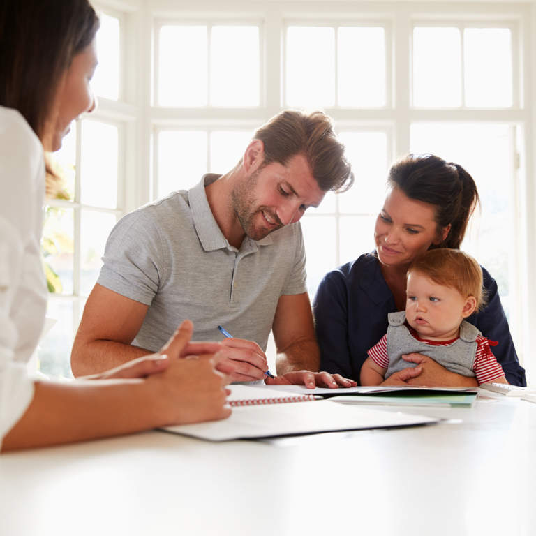 Couple with a baby and the father signing financial documents with a financial advisor.