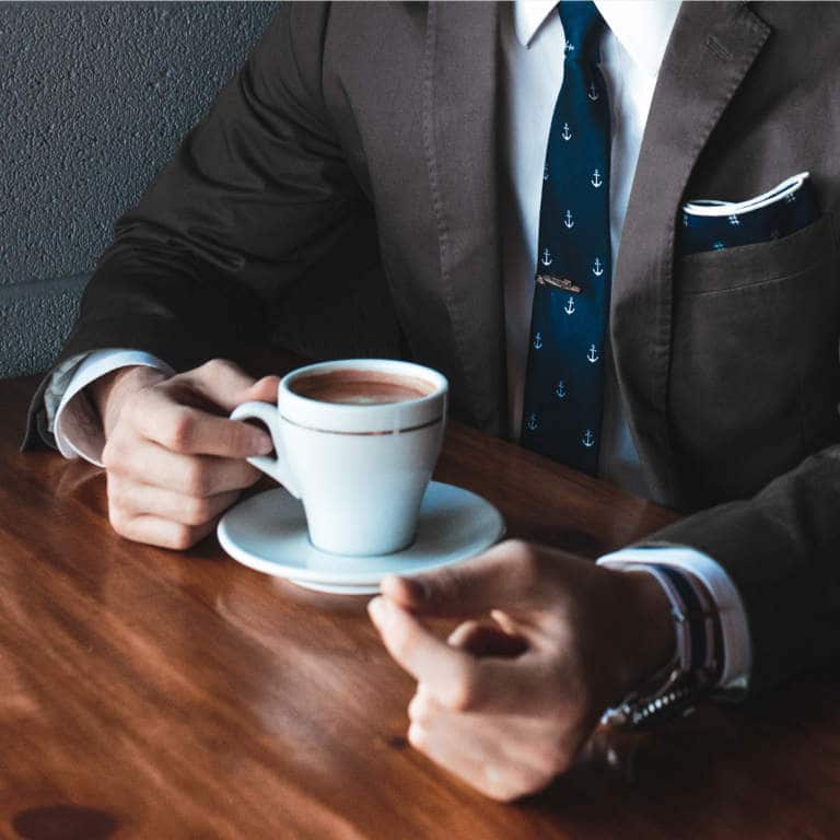A man in a smart suit sitting at a table having coffee.