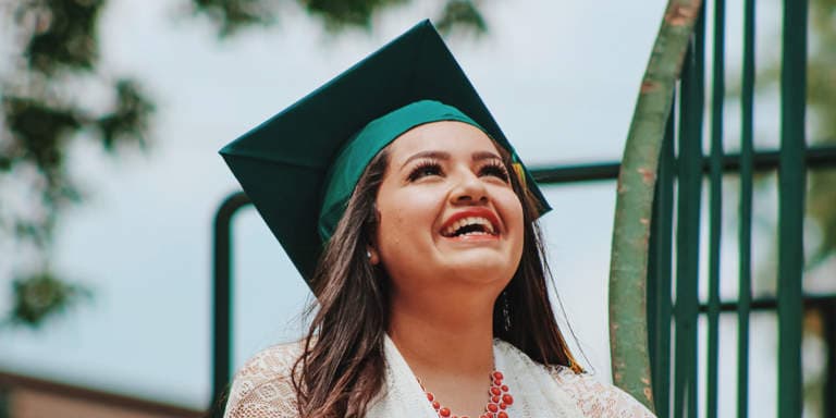 Young lady wearing a graduation hat looking at the sky with a broad smile.