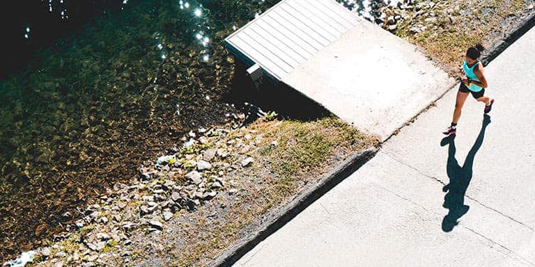 A woman wearing shorts and a turquoise training gear top, keeping active by running on the pavement next to a clear dam.