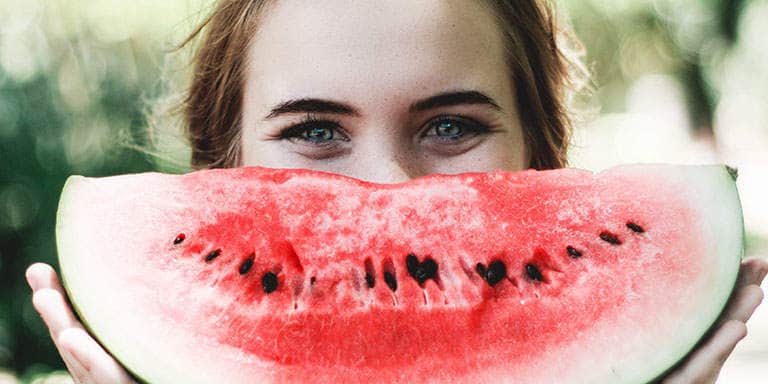 A young woman smiling and holding a sliced watermelon in front of her face to mimic a huge red smile.