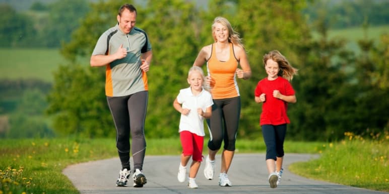 An energetic family of 4 - a mother, father, and 2 young children jogging on a country path.
