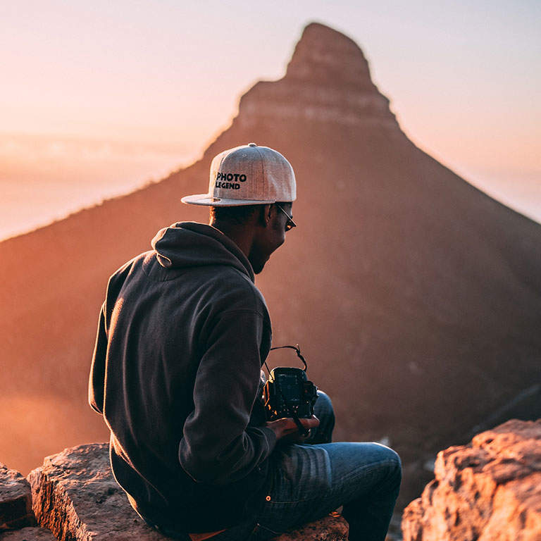 Young man with sunglasses, cap and hoodie exercising and taking photo's with his camera in a mountainous area in the early morning.
