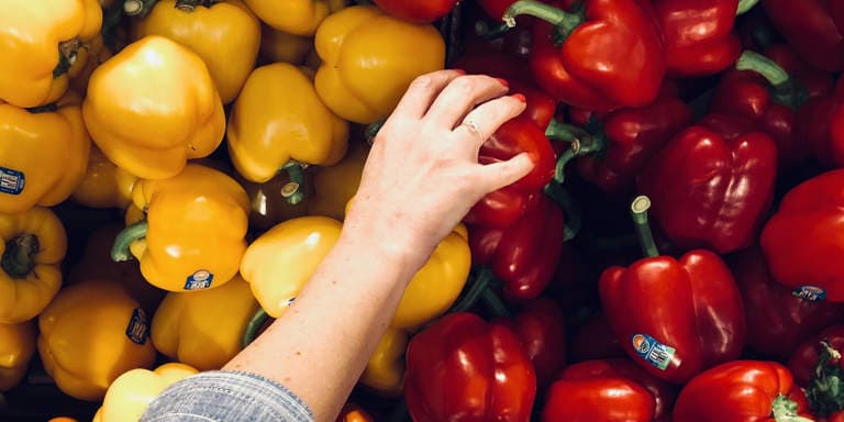 Red and yellow fresh bell peppers with a woman’s hand choosing a red bell pepper at the market.