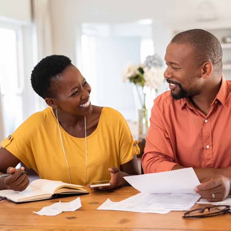 A husband and wife look at each other smiling while reviewing their tax and retirement and investment goals.