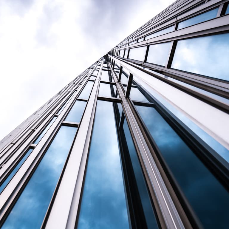A vertical look at a tall building made from glass and metal against a backdrop of a cloudy sky.